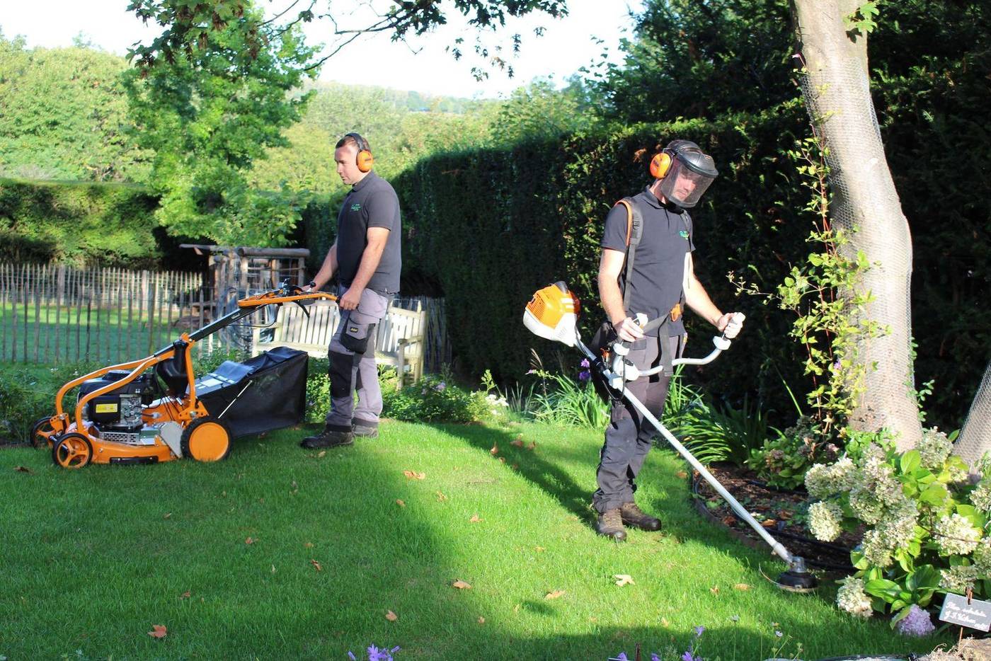 Deux opérateurs avec tondeuse et coupe-bordure dans un jardin